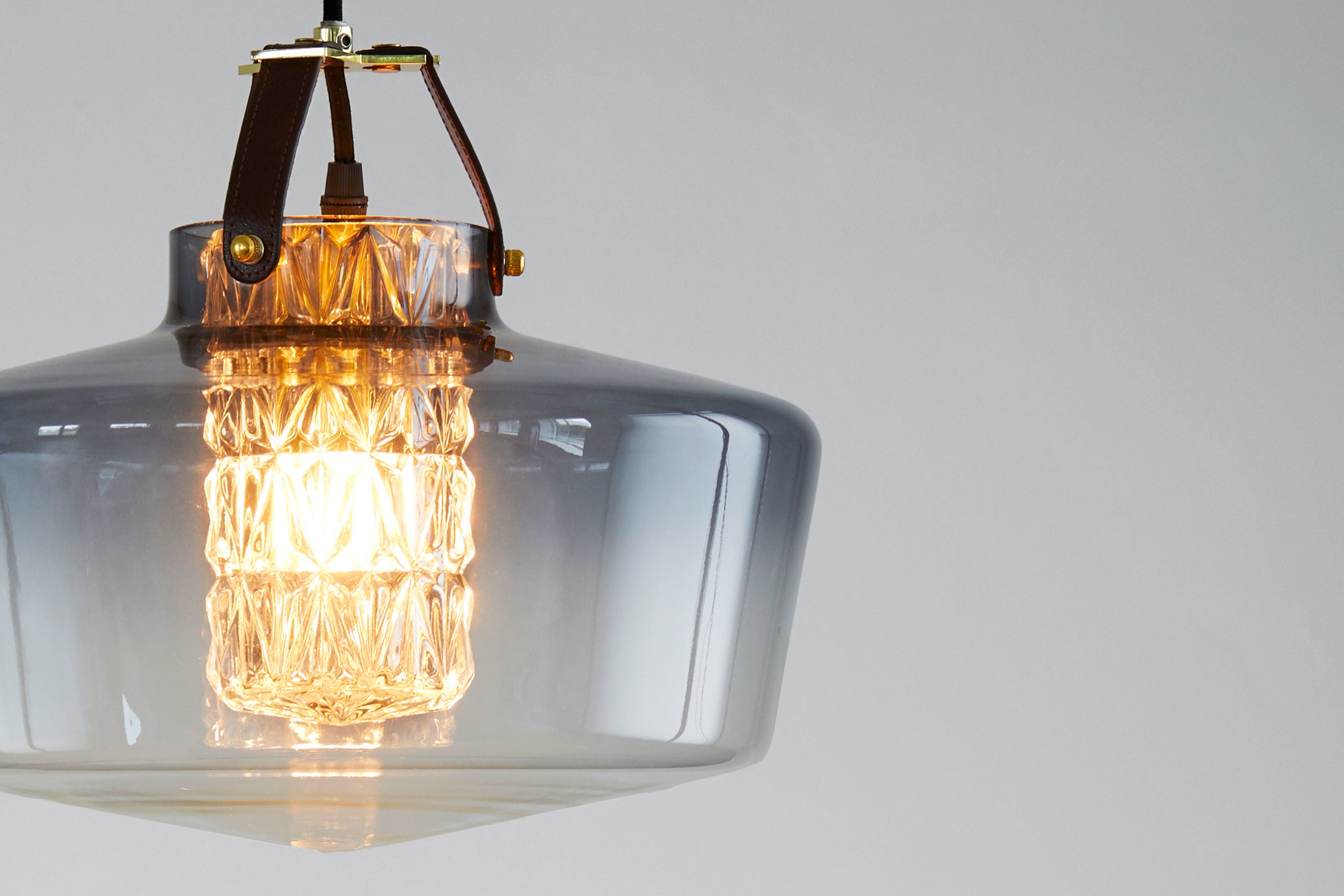 Lampen har en røgfarvet glasskærm i mundblæst glas, et facetslebet cylinderrør samt unikke detaljer i bl.a. læder.