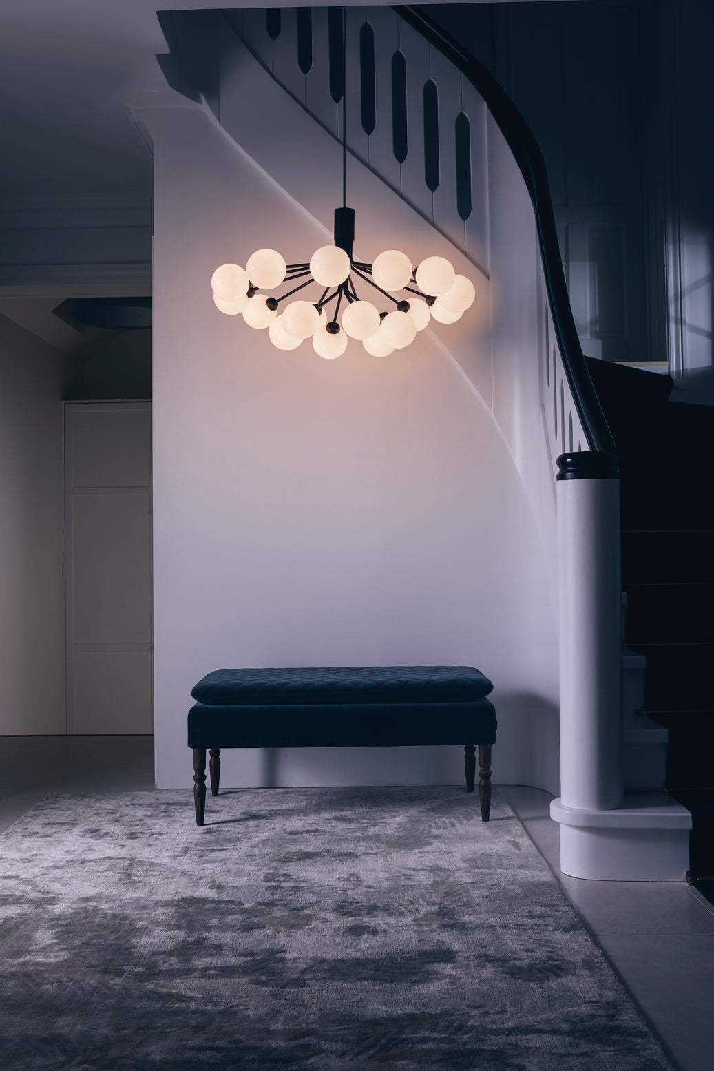 Lysekrone bestående af runde skærme i opalglas samt sort krone, i hall over bænk