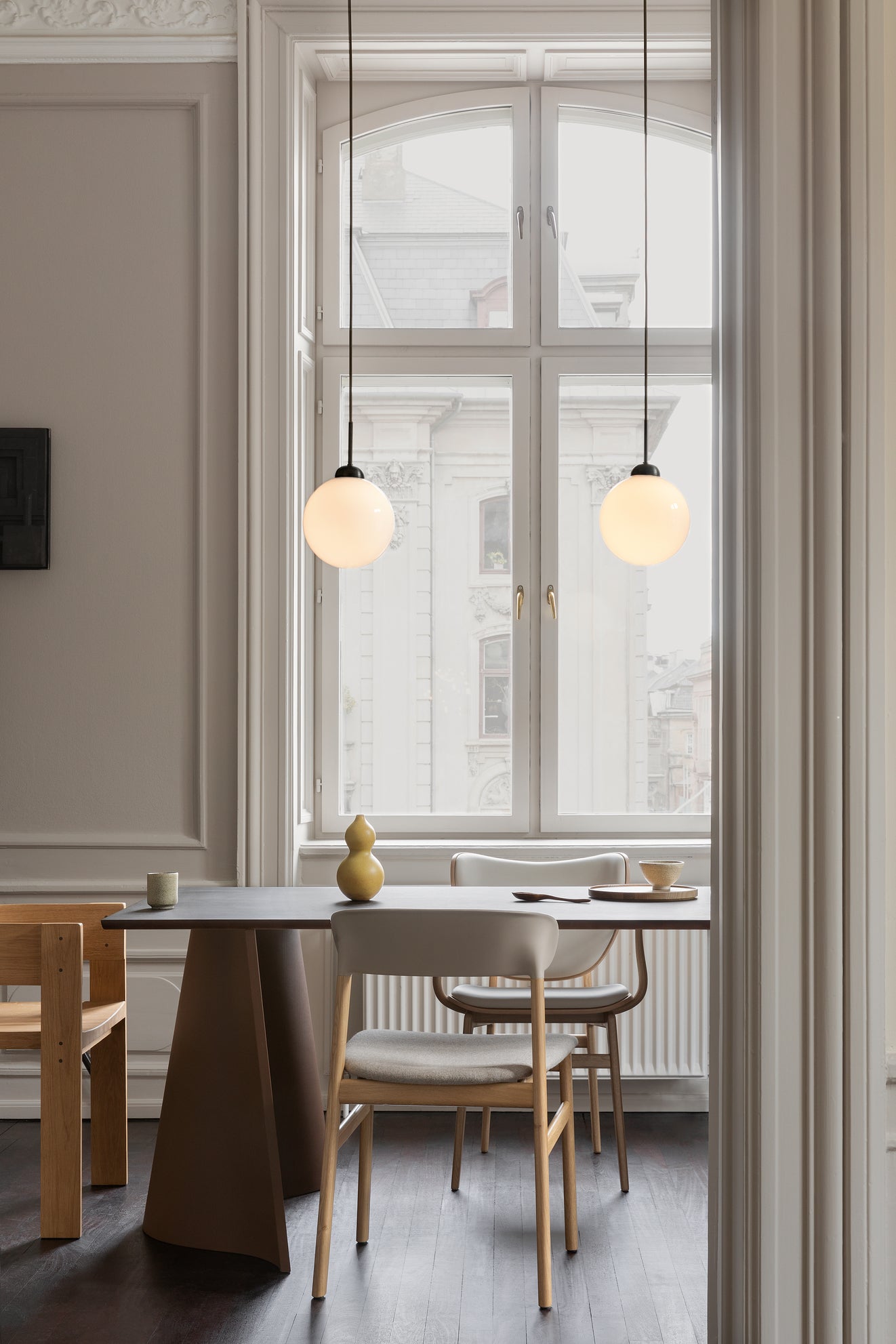 To pendler bestående af en rund skærm af opalglas og sort fatning samt ophæng, hængende over spisebord i dagligstuemiljø