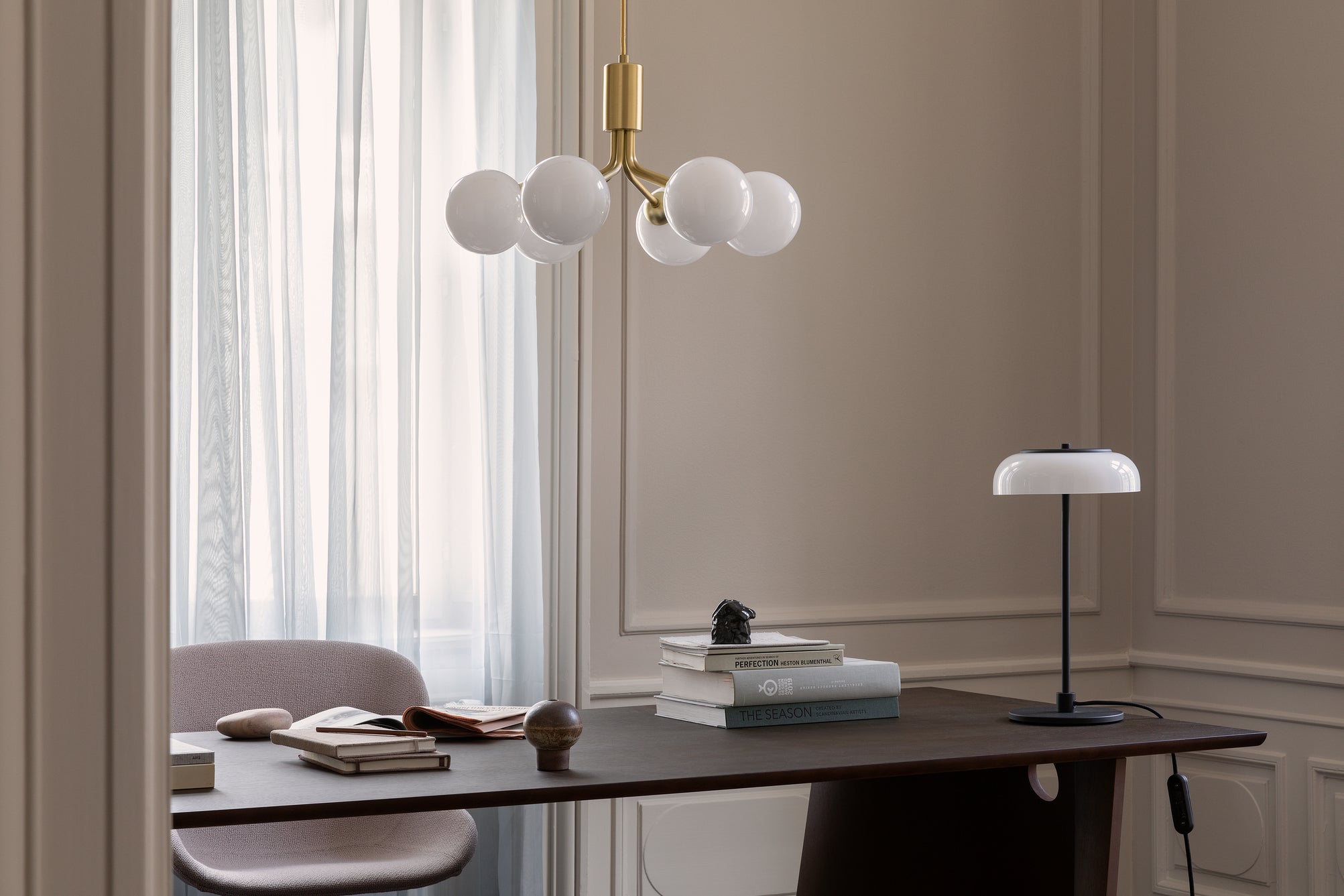 Lysekrone bestående af runde skærme i opalglas samt messingfarvet krone, over skrivebord