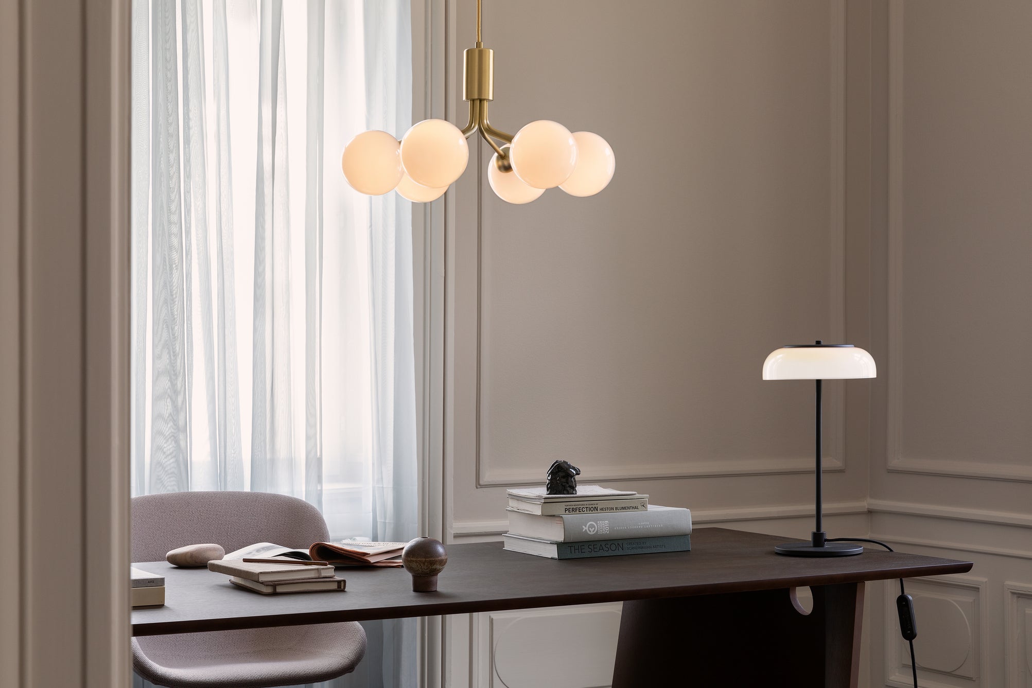 Lysekrone bestående af runde skærme i opalglas samt messingfarvet krone, over skrivebord