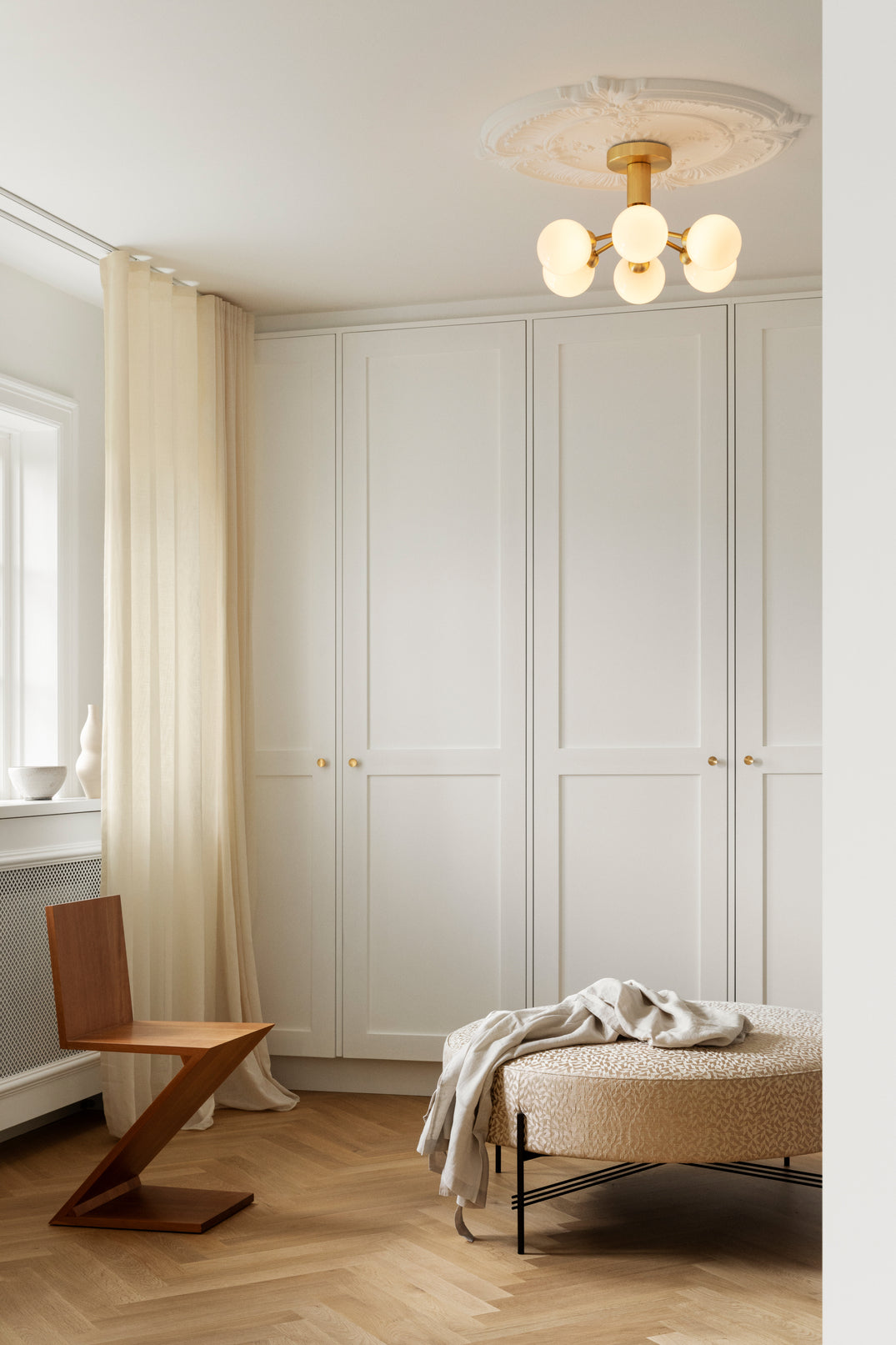 Lysekrone bestående af runde skærme i opalglas samt messingfarvet krone, i dagligstuemiljø