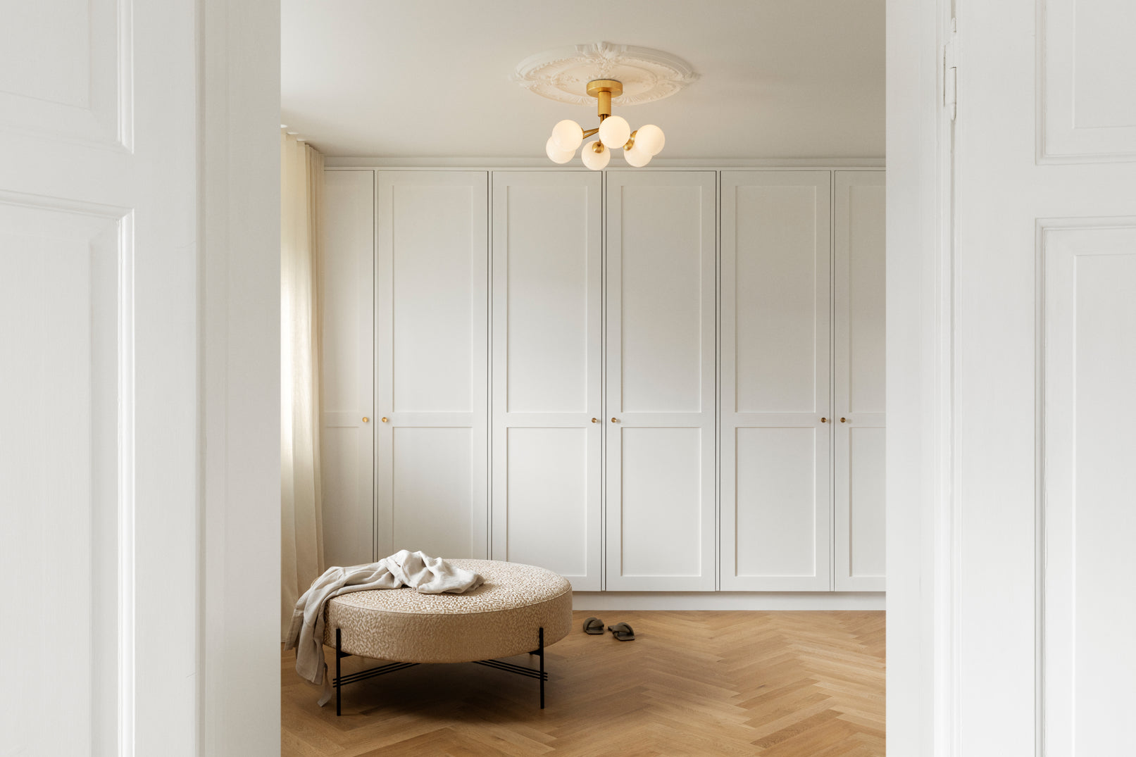 Lysekrone bestående af runde skærme i opalglas samt messingfarvet krone, i soveværelsesmiljø