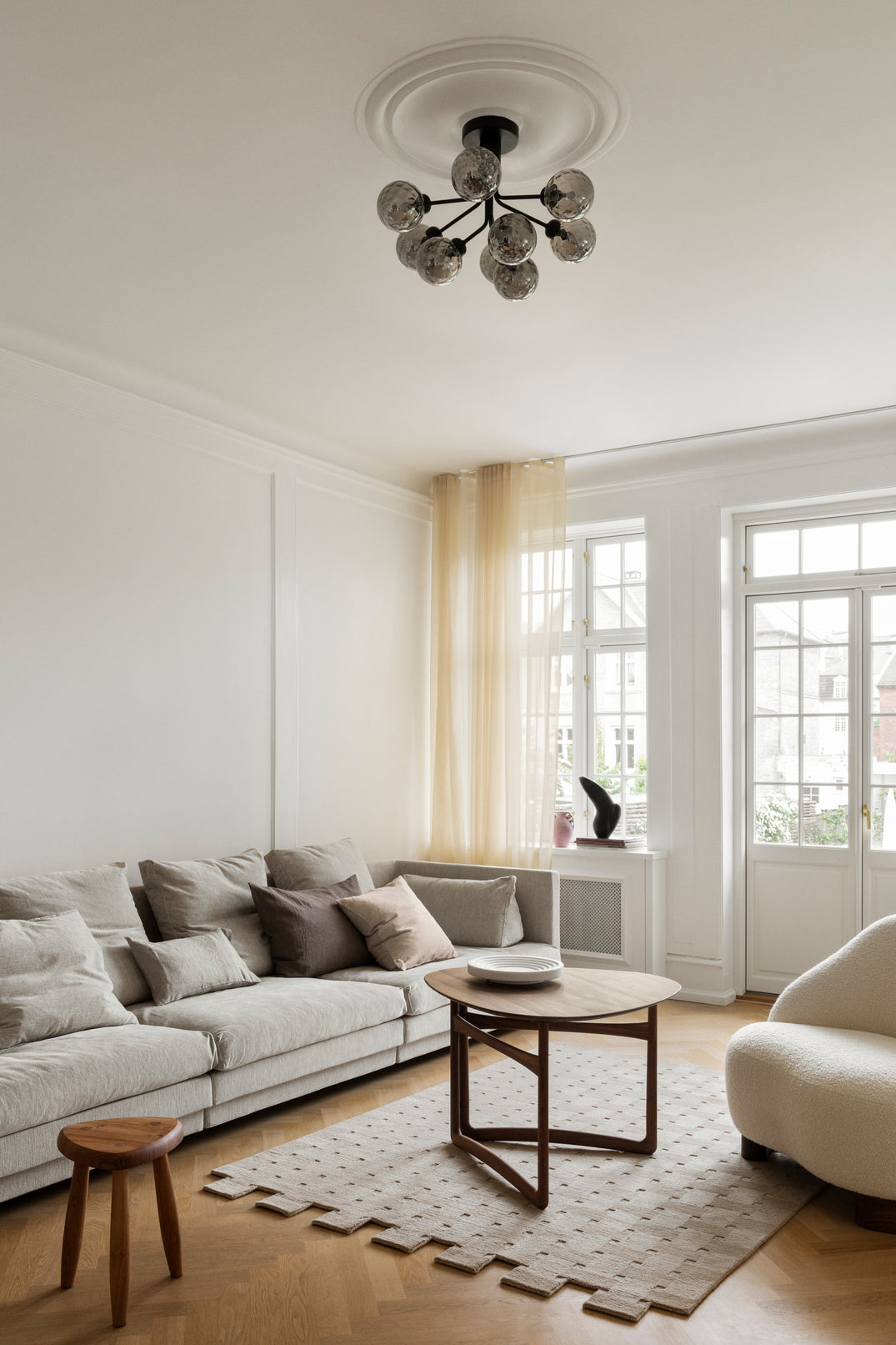 Lysekrone bestående af runde skærme i røgfarvet optikglas samt sort krone, i dagligstuemiljø