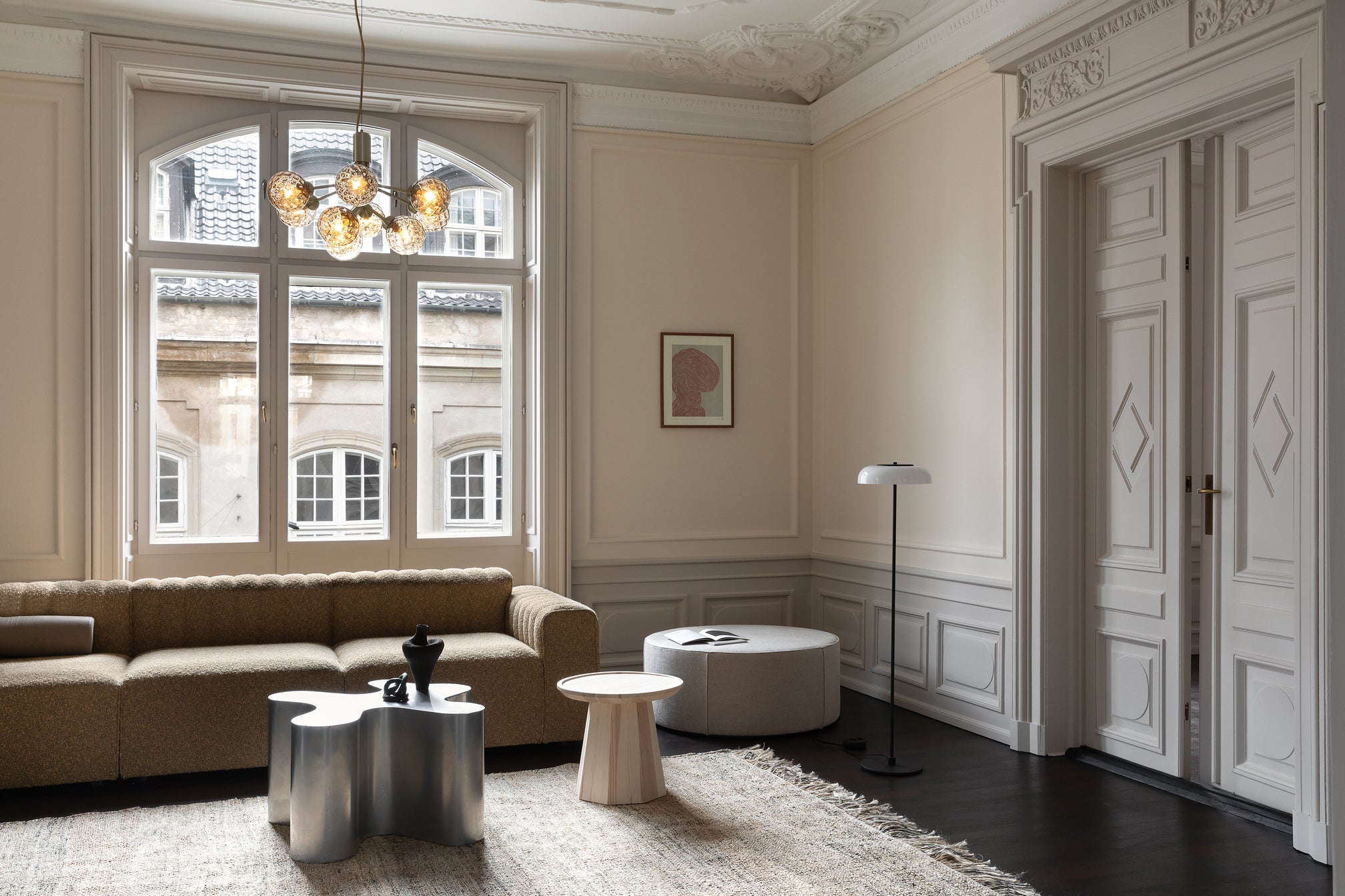 Lysekrone bestående af runde skærme i gyldent optikglas samt messingfarvet krone, i dagligstuemiljø