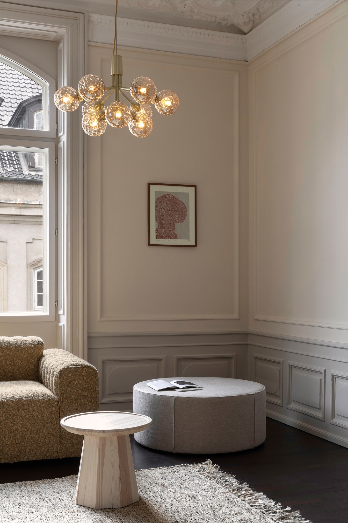 Lysekrone bestående af runde skærme i gyldent optikglas samt messingfarvet krone, i dagligstuemiljø