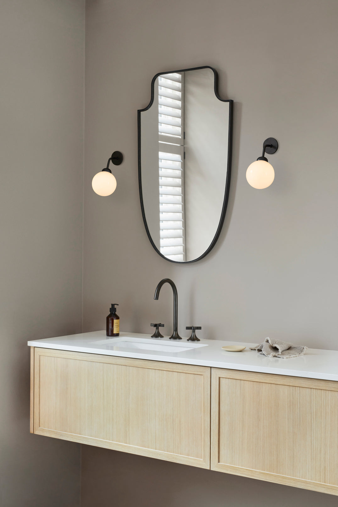 To væglamper med rund skærm af opalglas og sort stel, på badeværelse