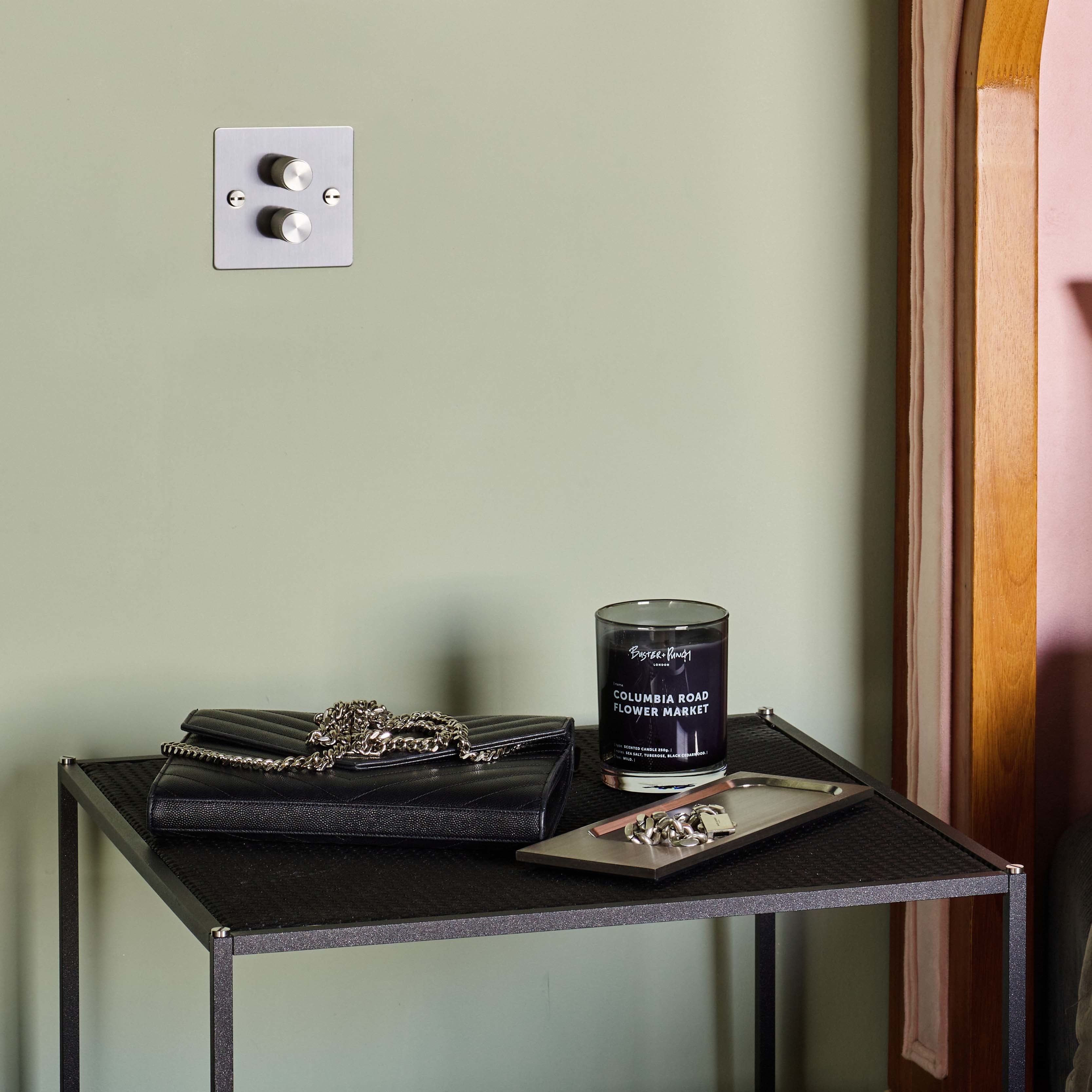 Duftlys af sort voks i røgfarvet glas med tændt flamme, på sidebord.