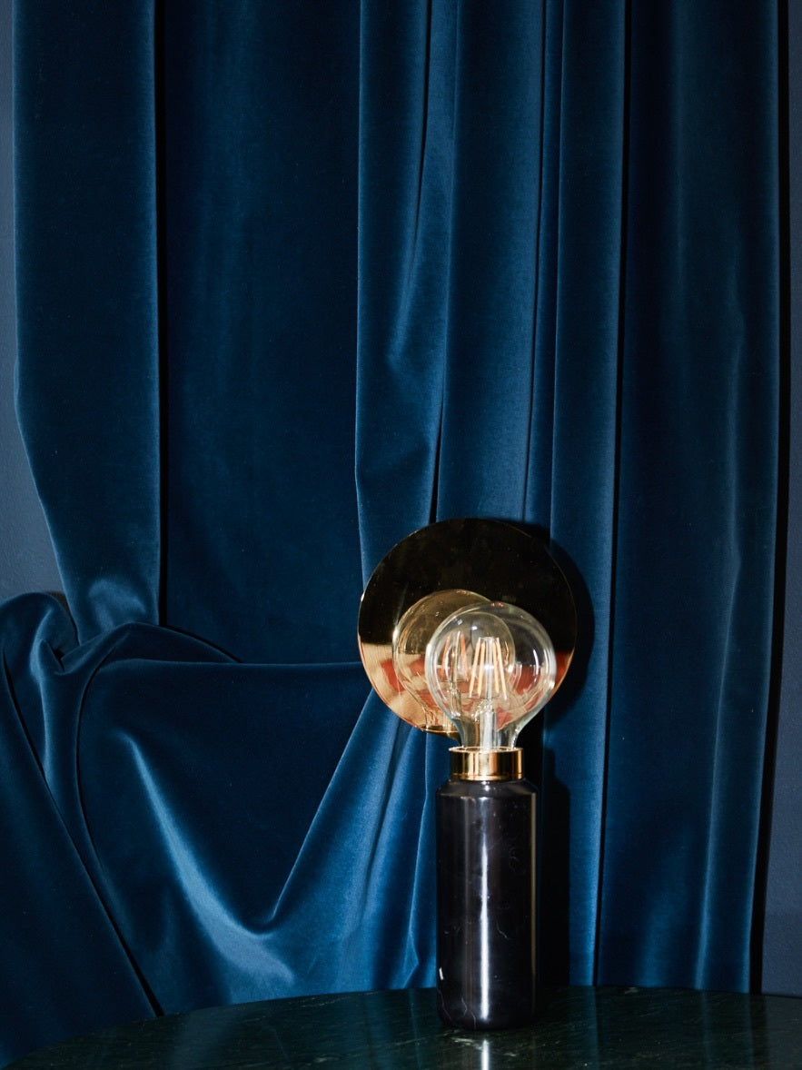 På billedet ses bordlampen med navnet blindspot. Lampen består af en høj cylinderformet fod i sort marmor. Derudover har lampen en messing fatning og en rund messing plade, hvor pæren spejles is. Pladen dækker desuden for pæren, så denne ikke blænder. Pæren er inspireret af den klassiske glødepære men er en LED (købes separat).