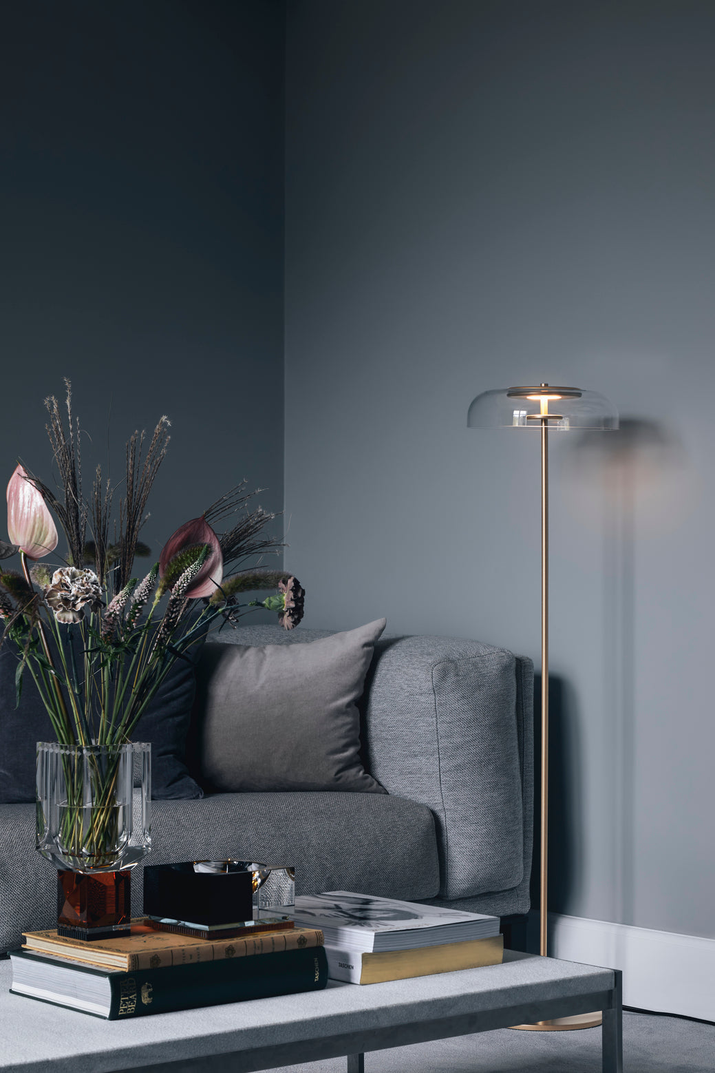 Gulvlampe med gyldent stel og fatning samt klar glasskærm, i dagligstuemiljø