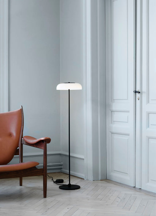 Gulvlampe med sort stel og fatning samt glasskærm i opalglas, i dagligstuemiljø