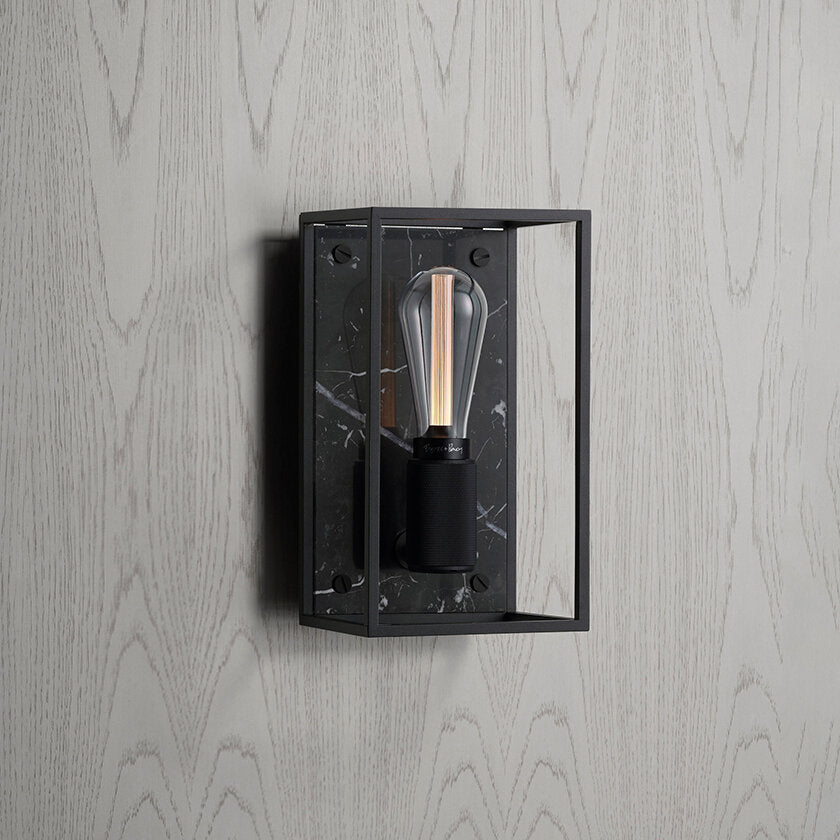 Buster and Punch caged wall lamp medium i sort metal med bagpanel i sort marmor.