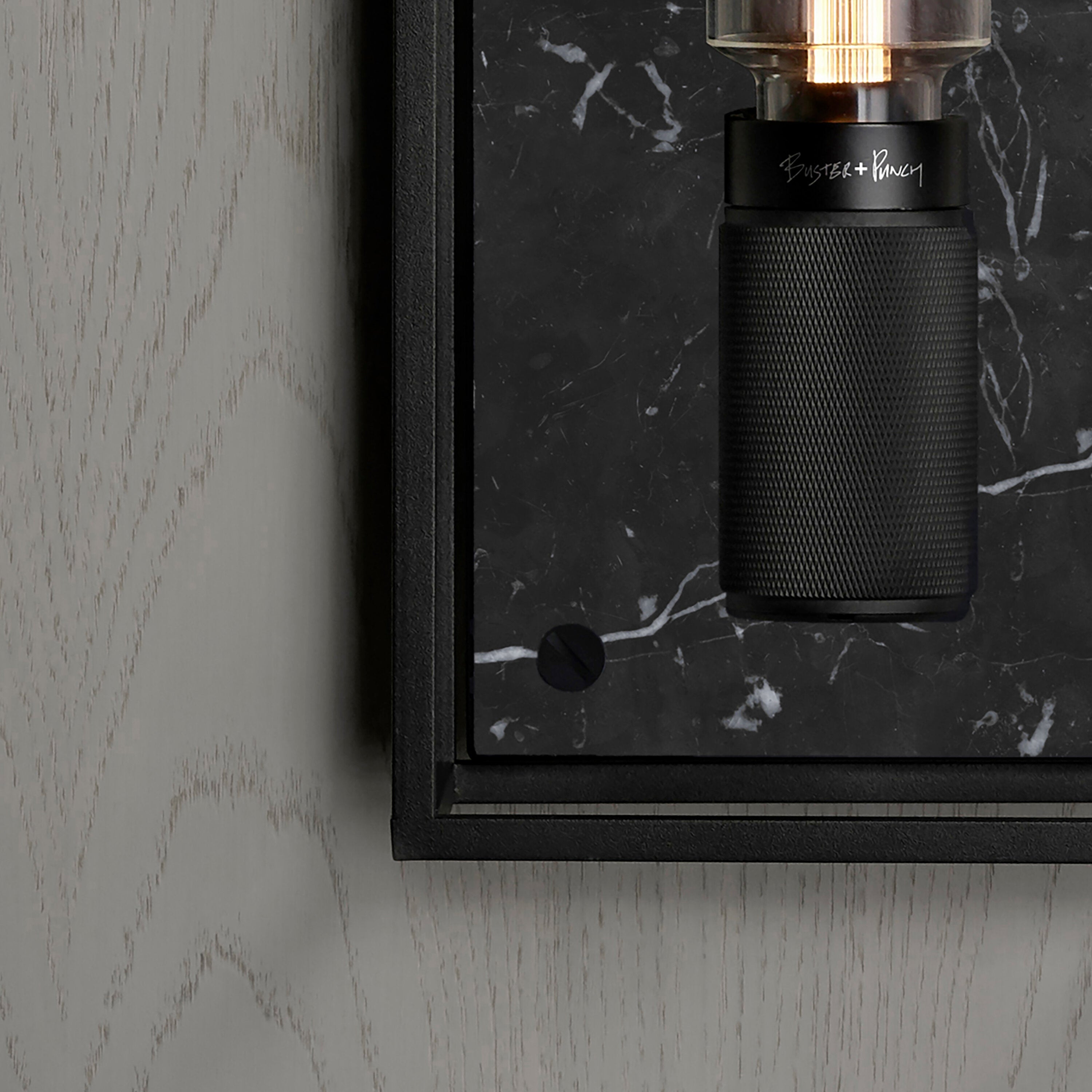 Buster and Punch caged wall lamp medium i sort metal med bagpanel i sort marmor.