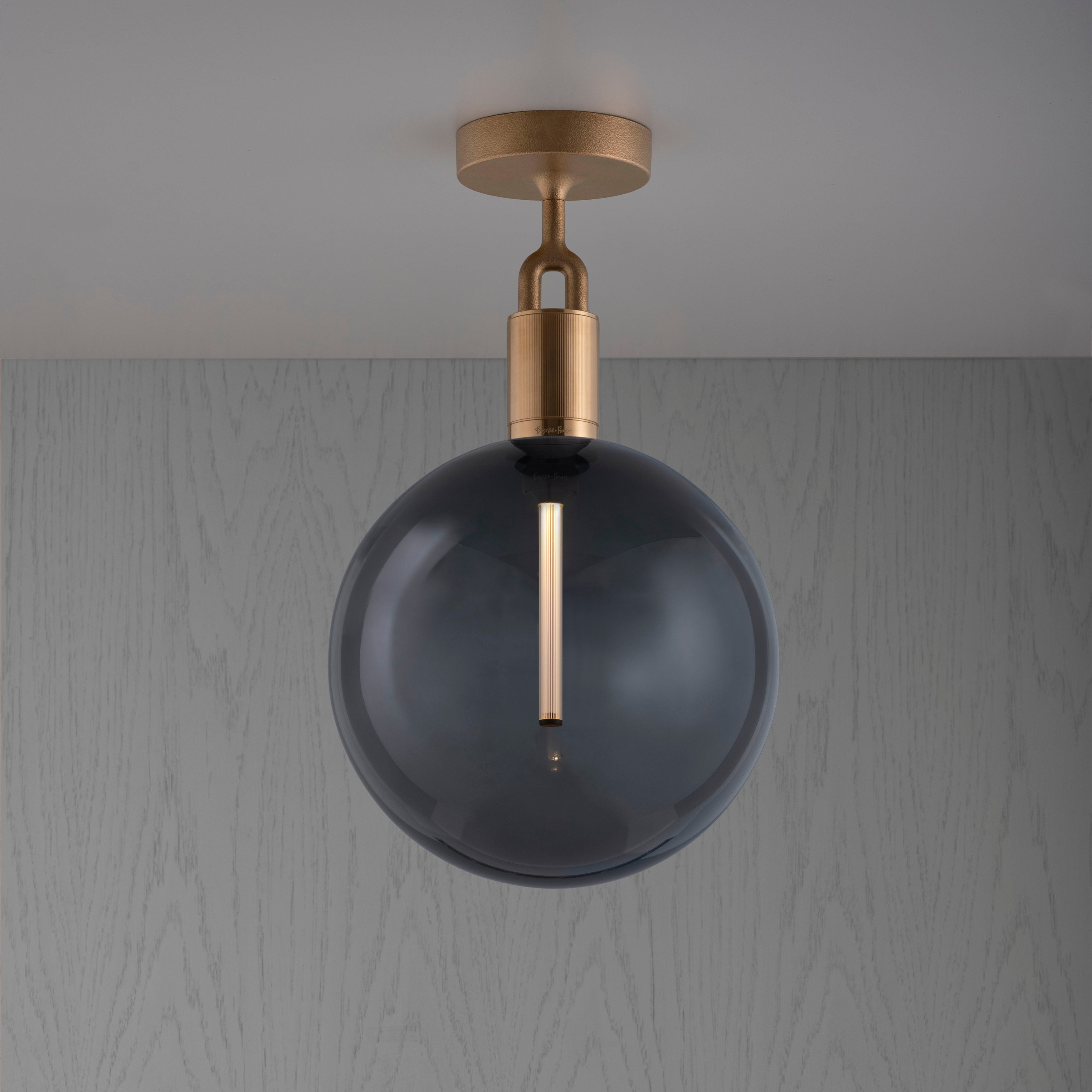 Loftlampe med rund skærm og messingfatning, på baggrund af gråt træ.