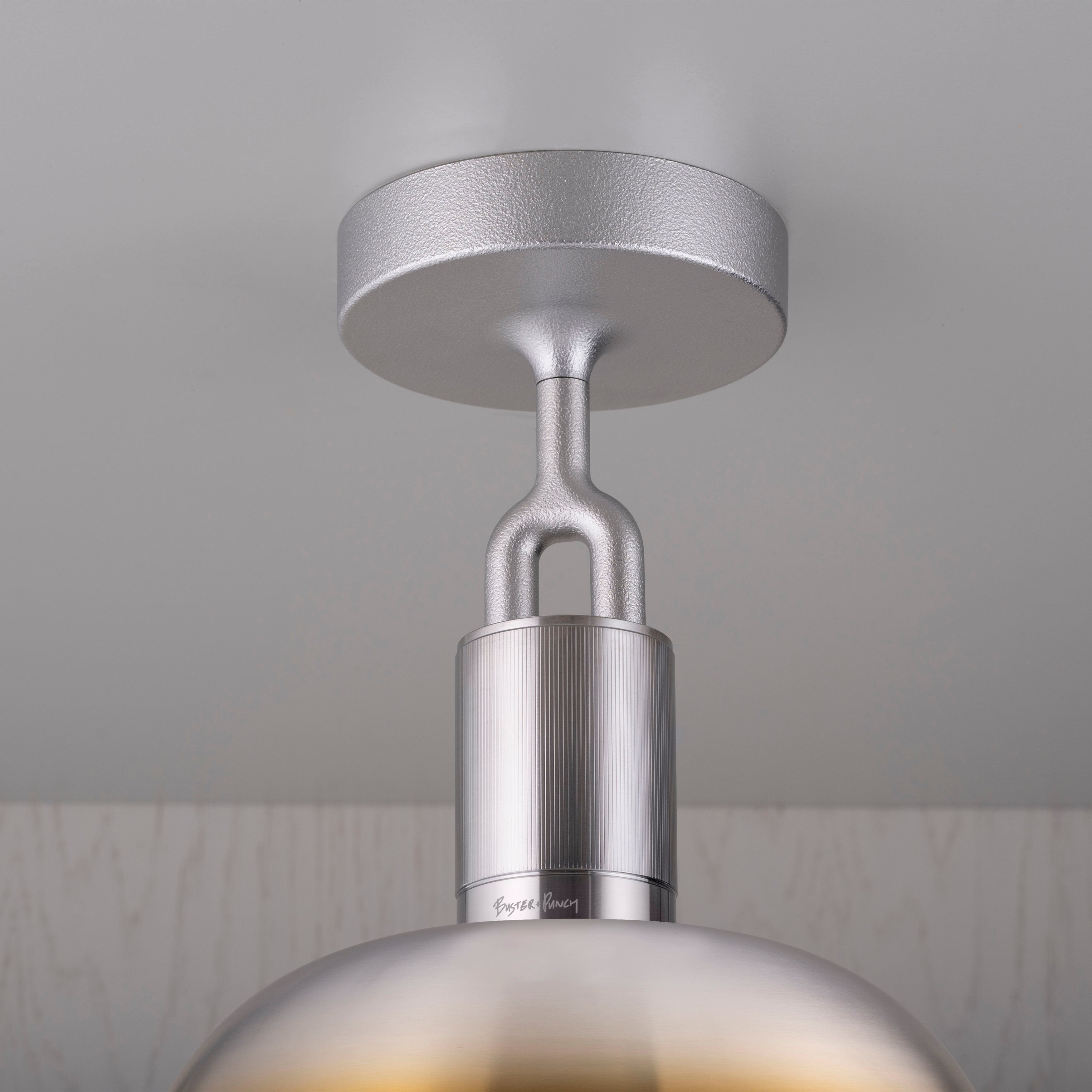 Detaljebillede af fatning samt skærm af stål og brændt stål, på grå baggrund.