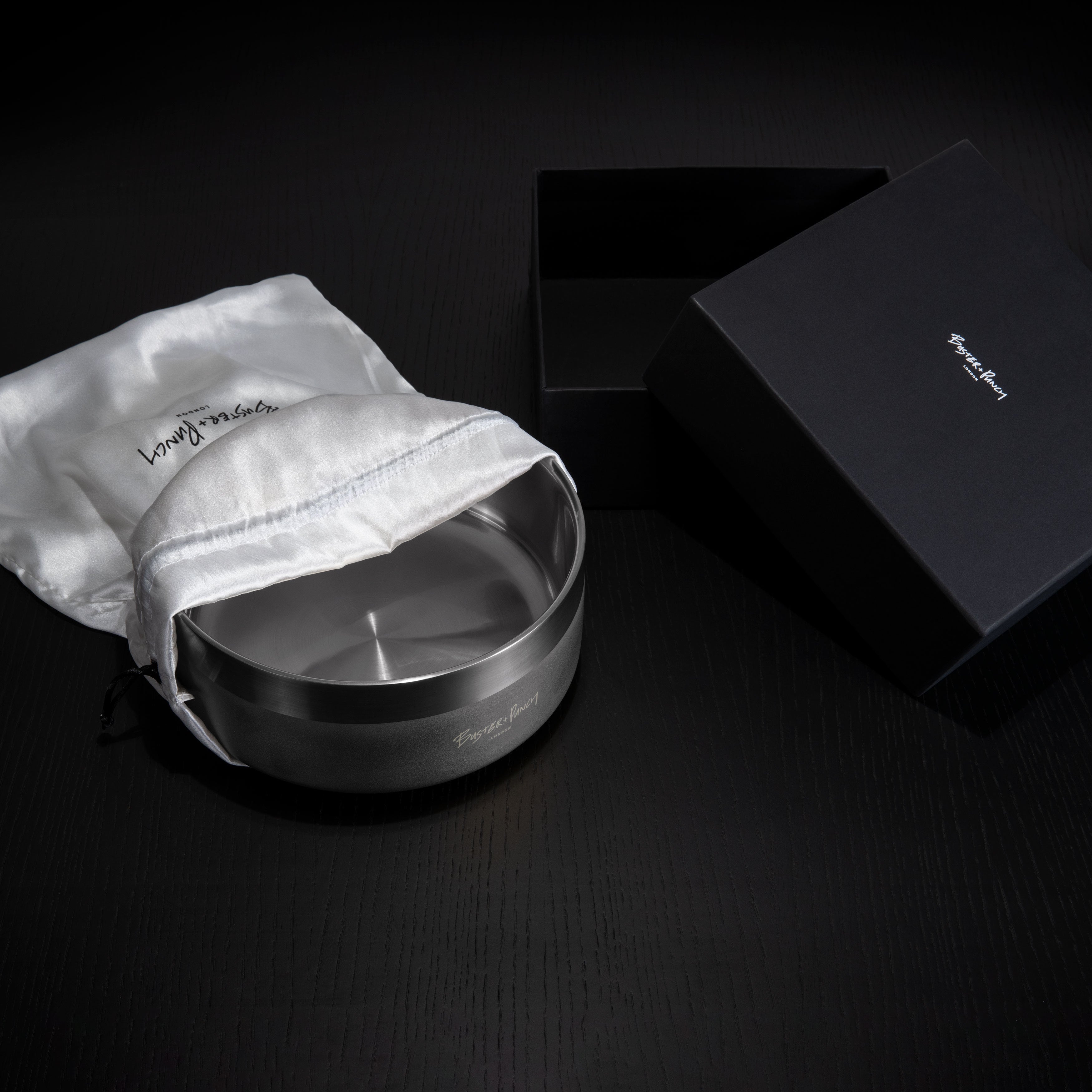 Æske indeholdende hundeskål i stål med gun metal finish, på sort træbord.