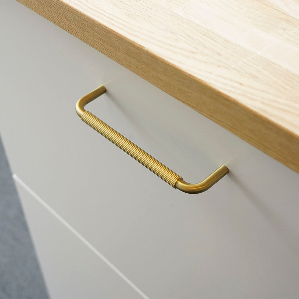 Køkken/bøjlegreb i massiv messing med linjeret overflade monteret på en skuffefront