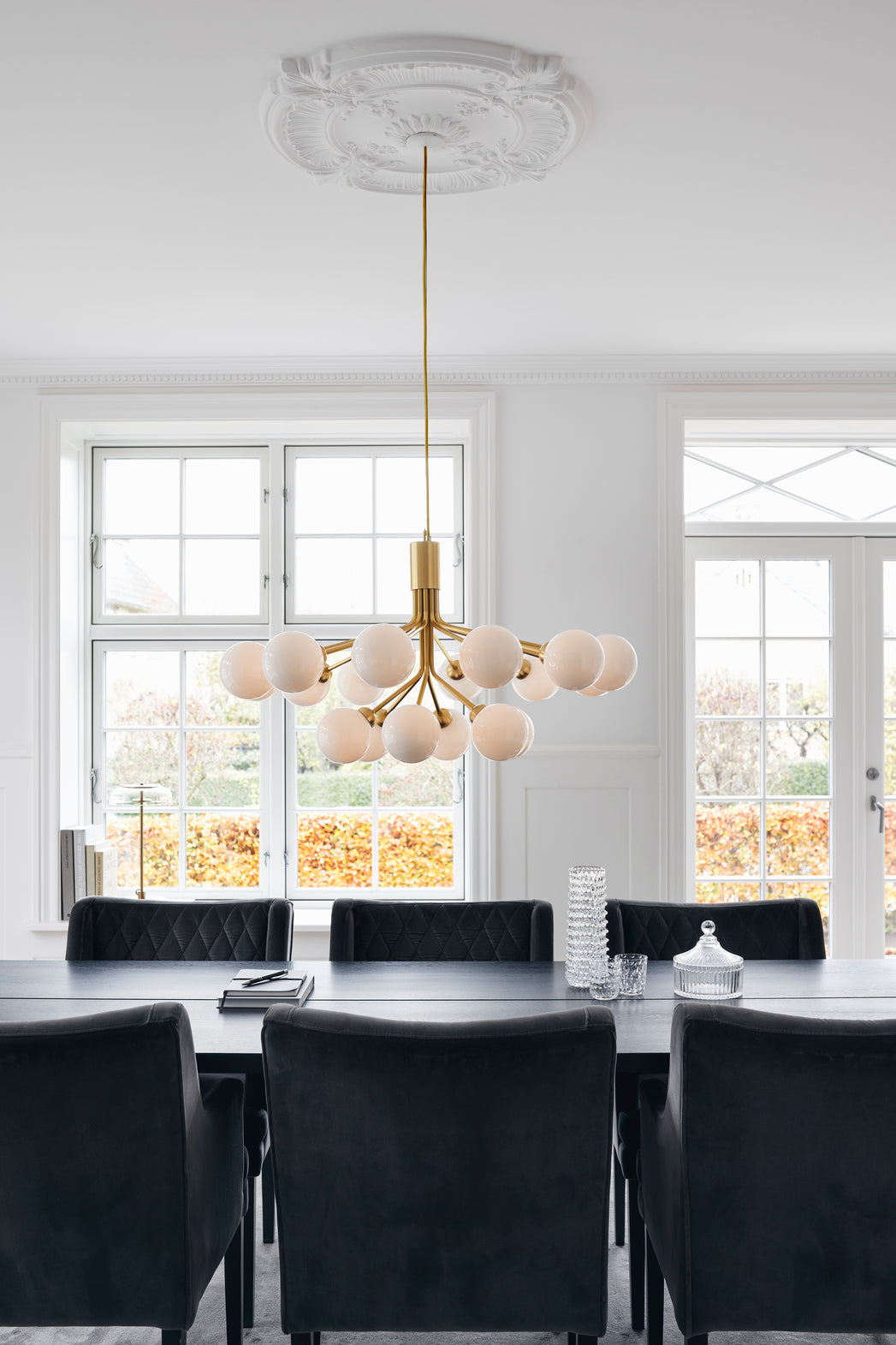 Lysekrone bestående af runde skærme i opalglas samt messingfarvet krone, over spisebord i dagligstuemiljø