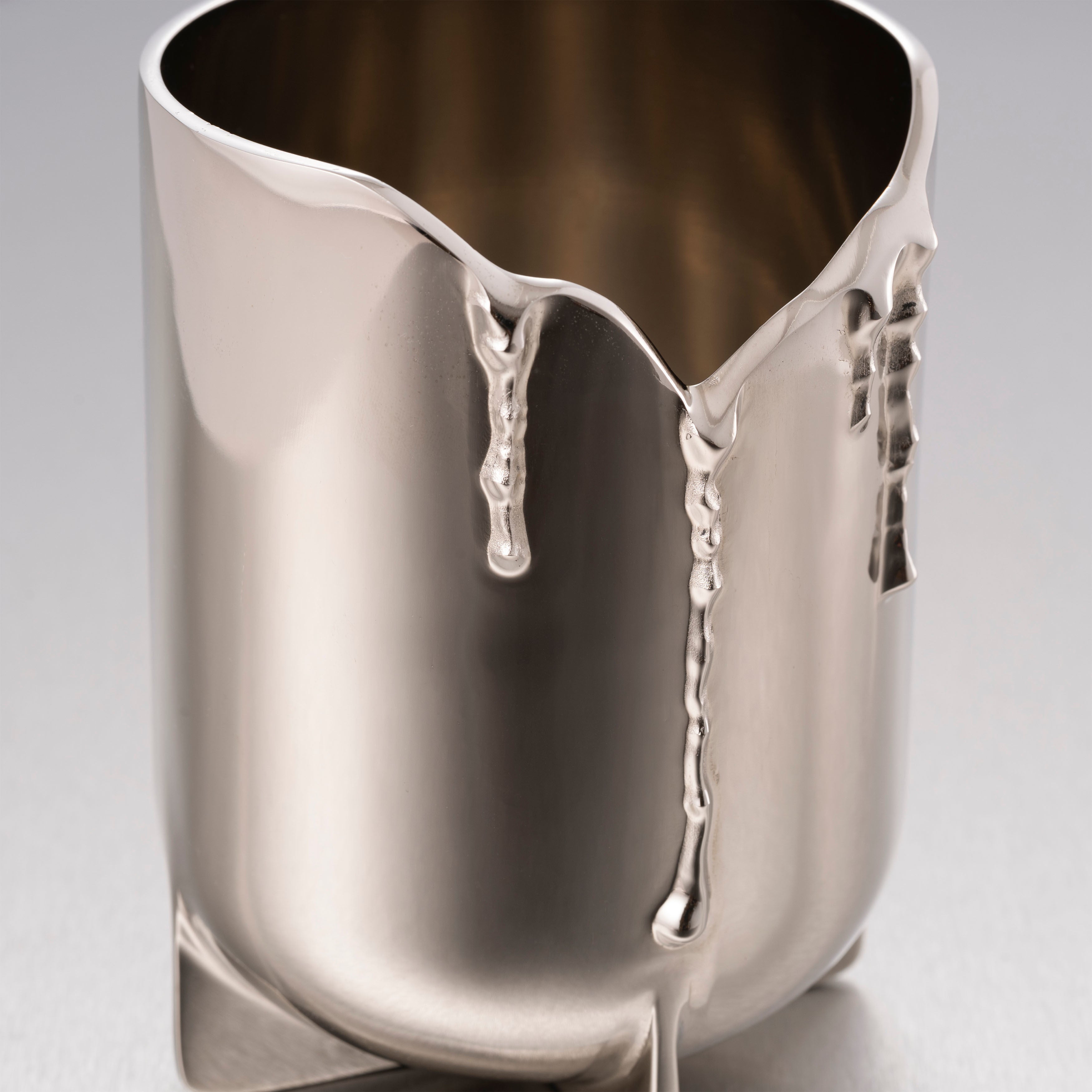 Detaljer af lysestage til duftlys i stål, på grå baggrund.