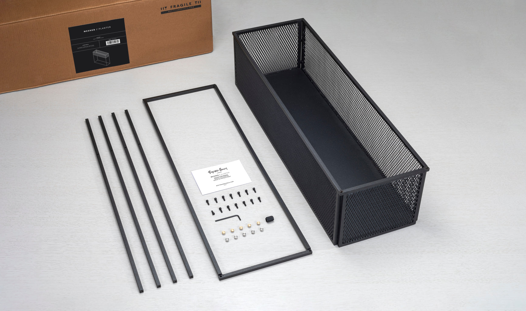 Firkantet og sort plantekasse i stålramme med meshed/hullet design på siderne. Der medfølger detaljer/skruer i både stål og messing.