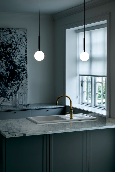 Pendel med rund skærm af opalglas og aflang grå fatning, over køkkenbord