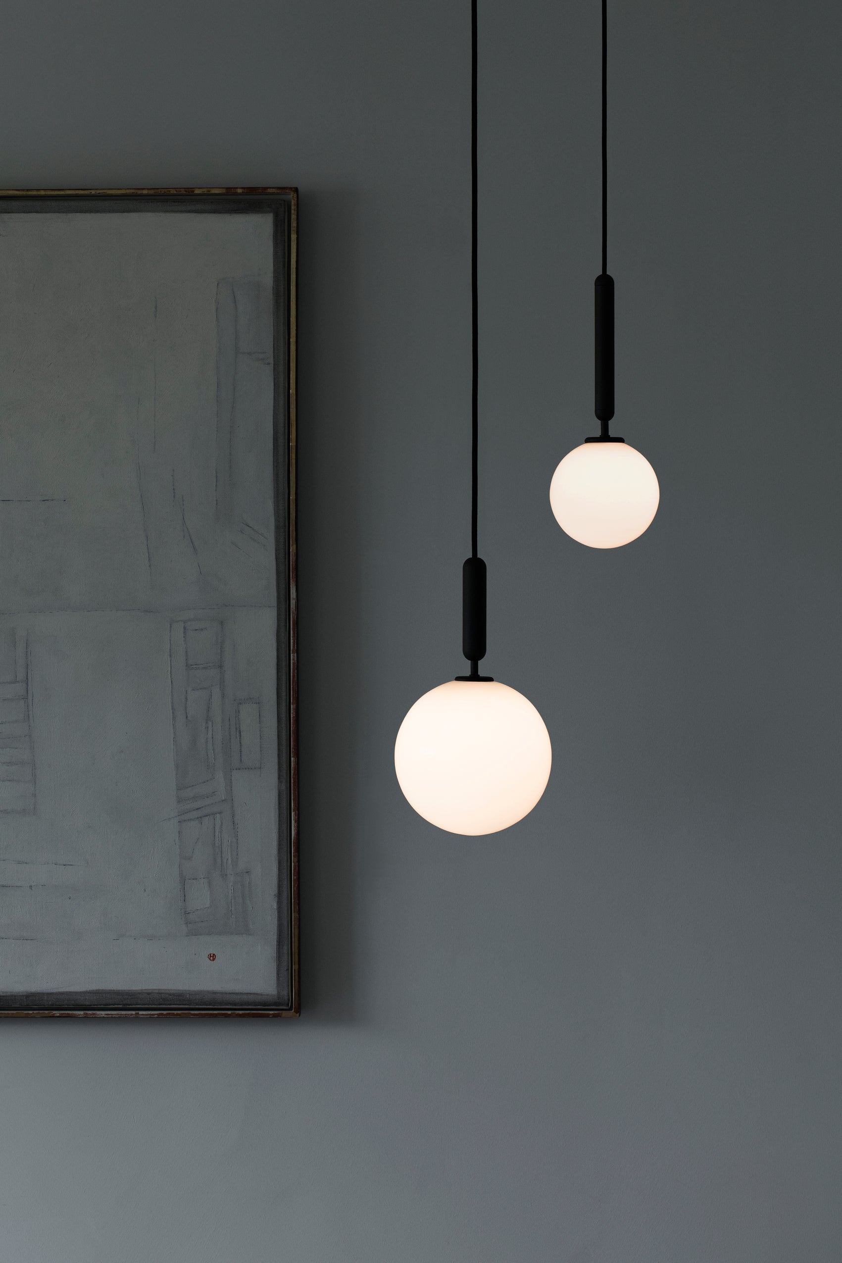 Pendel med rund skærm af opalglas og aflang grå fatning, i dagligstuemiljø