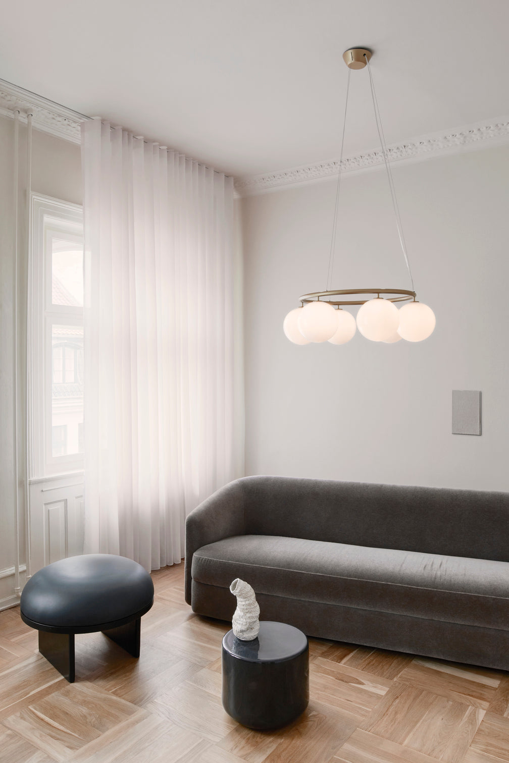 Lysekrone bestående af seks runde skærme i opalglas samt messingfarvet krone, i dagligstuemiljø