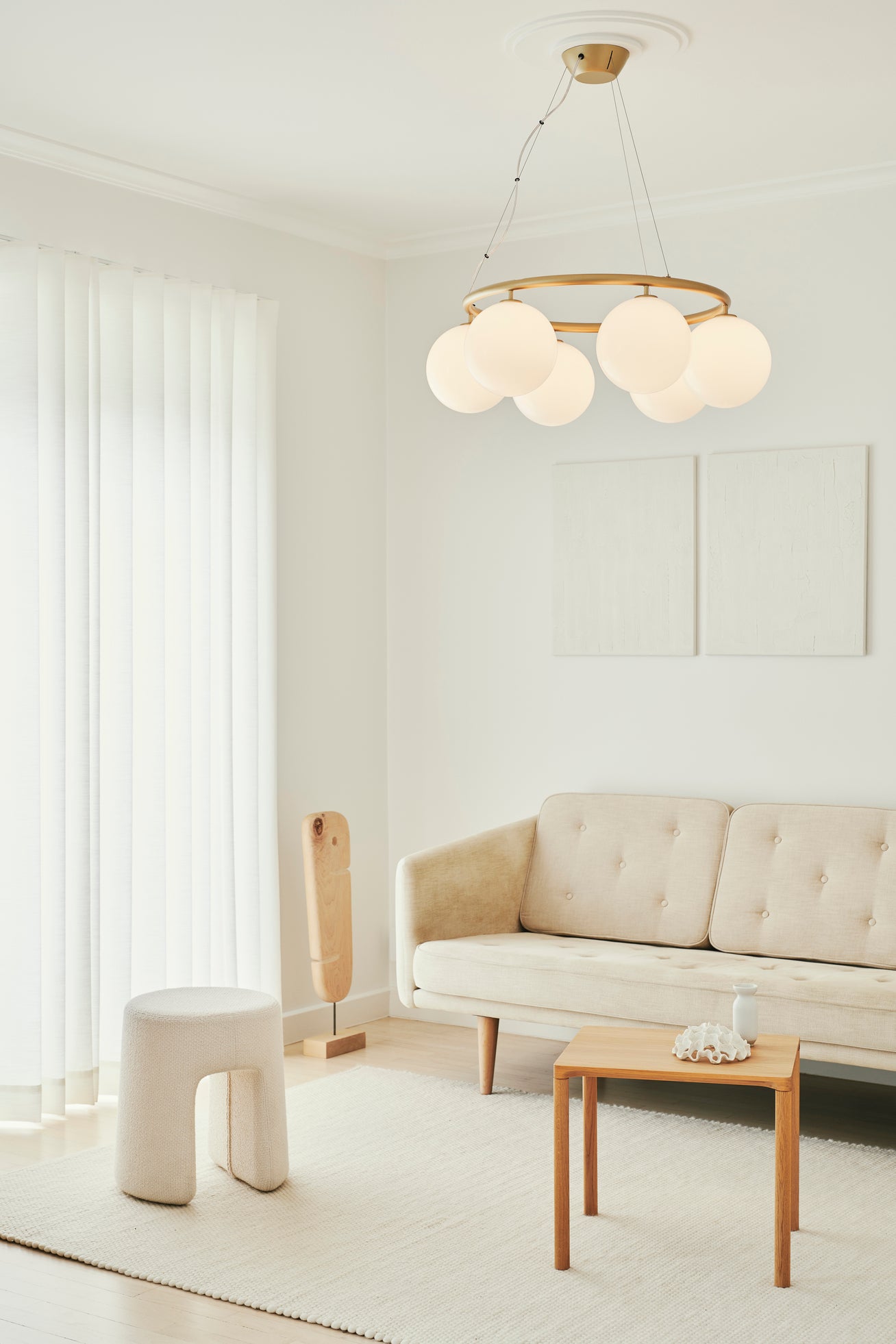 Lysekrone bestående af seks runde skærme i opalglas samt messingfarvet krone, i dagligstuemiljø