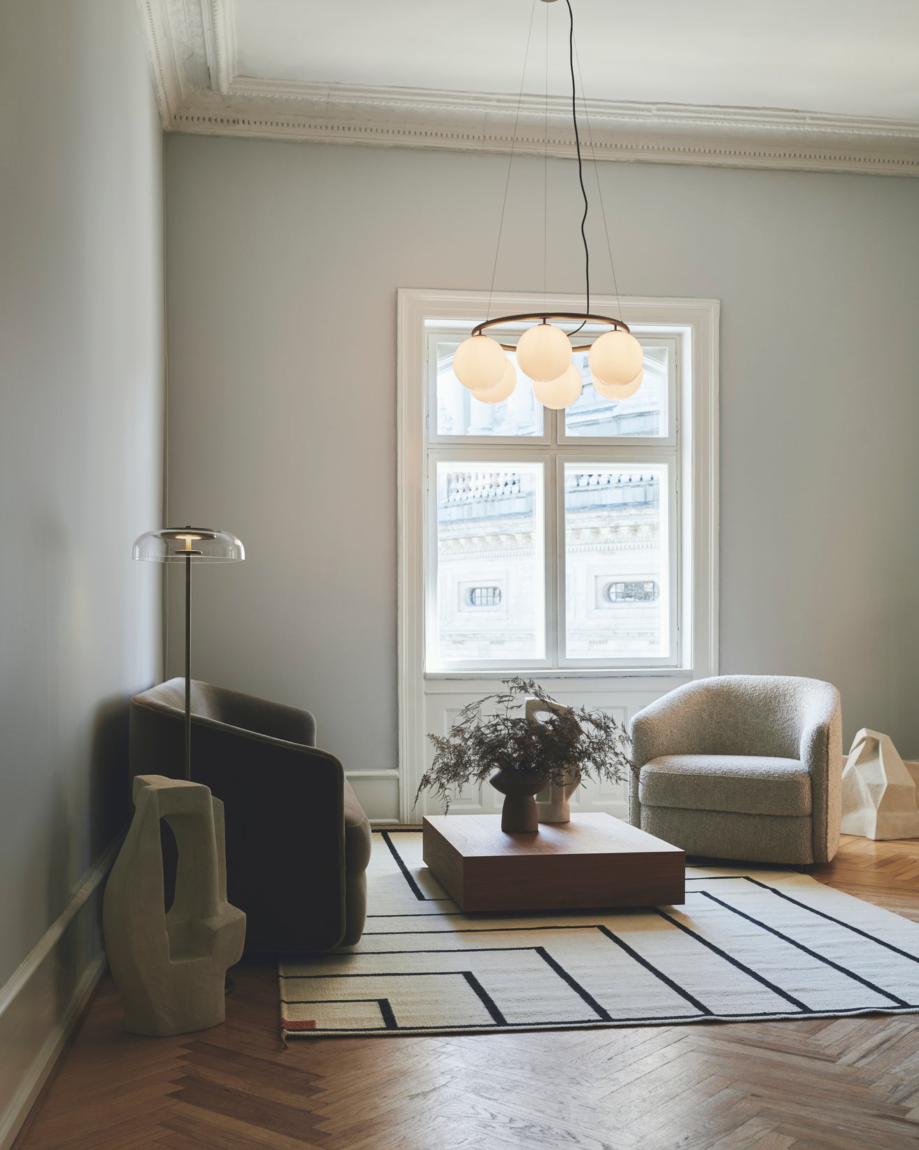 Lysekrone bestående af seks runde skærme i opalglas samt messingfarvet krone, i dagligstuemiljø