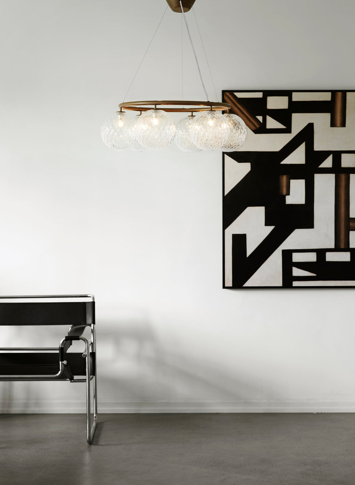 Lysekrone bestående af seks runde skærme i klart optikglas samt bruneret krone, i dagligstuemiljø