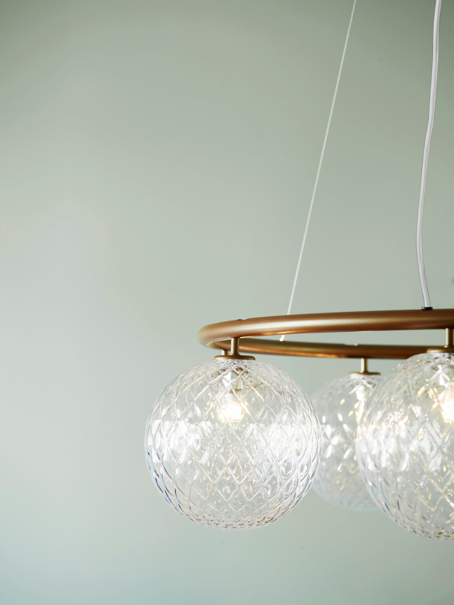 Close-up af lysekrone bestående af otte runde skærme i klart optikglas samt bruneret krone