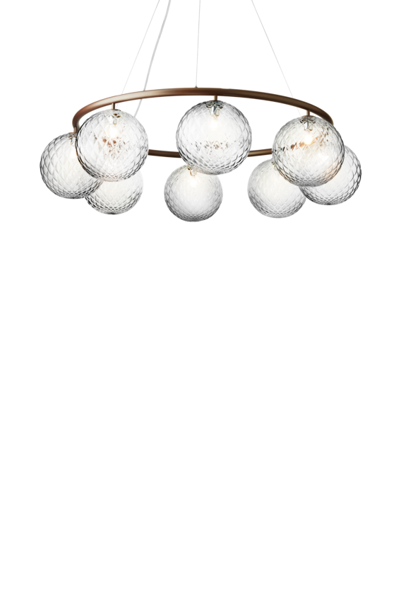 Lysekrone bestående af otte runde skærme i klart optikglas samt bruneret krone, på hvid baggrund