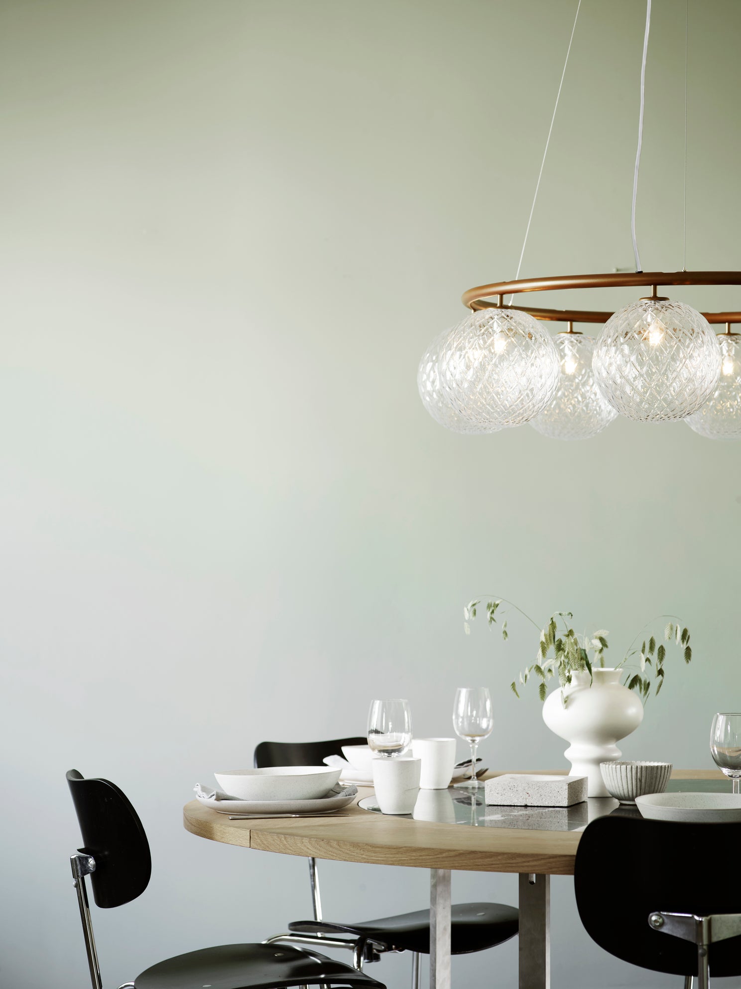 Lysekrone bestående af otte runde skærme i klart optikglas samt bruneret krone, hængende over spisebord