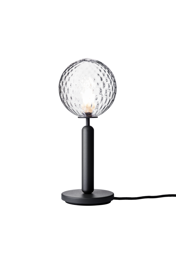 Bordlampe med rund skærm af klart optikglas og mørkegråt stel, på hvid baggrund