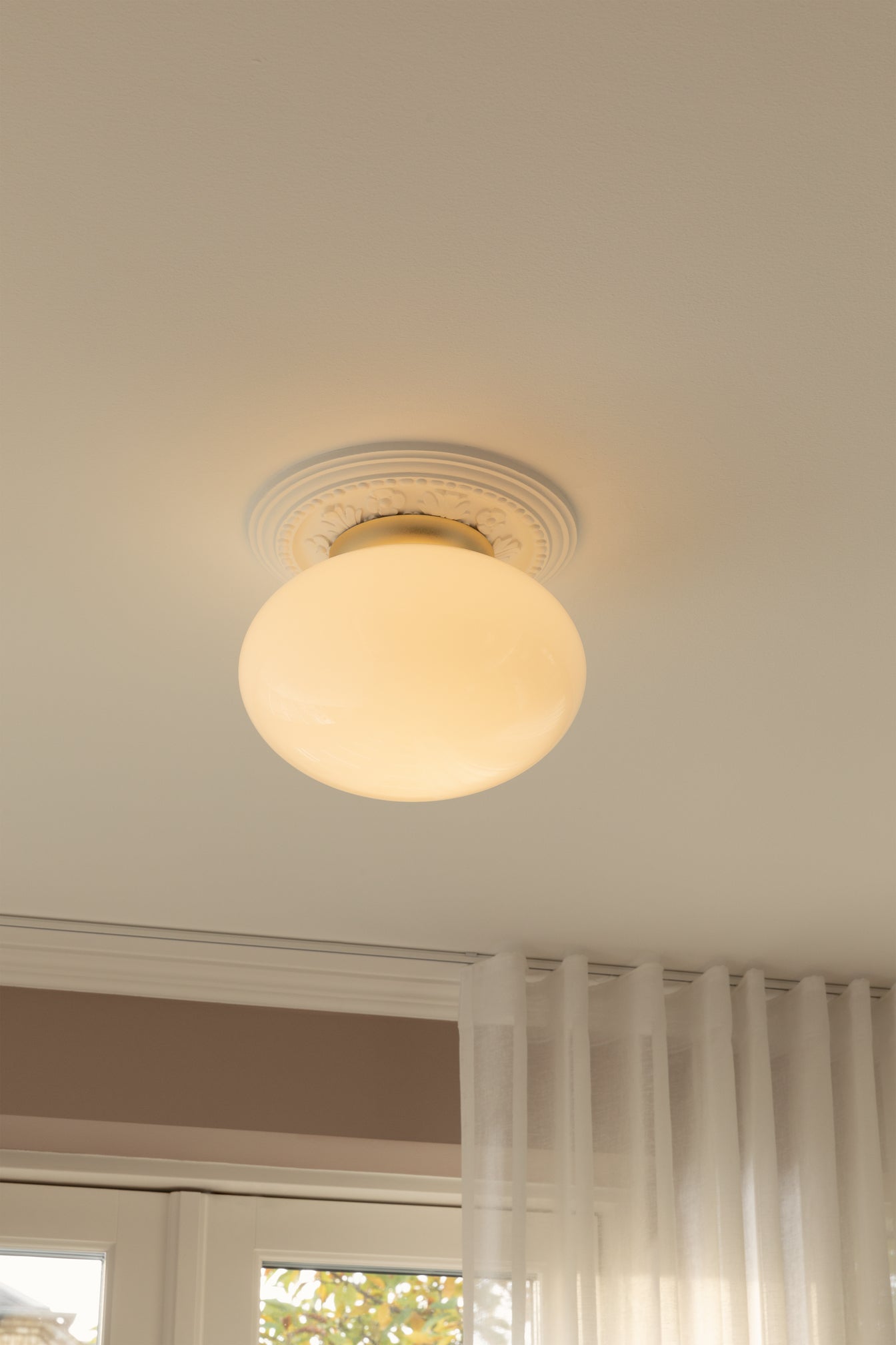 Loftlampe med messingfarvet fatning og skærm i opalglas, i dagligstuemiljø