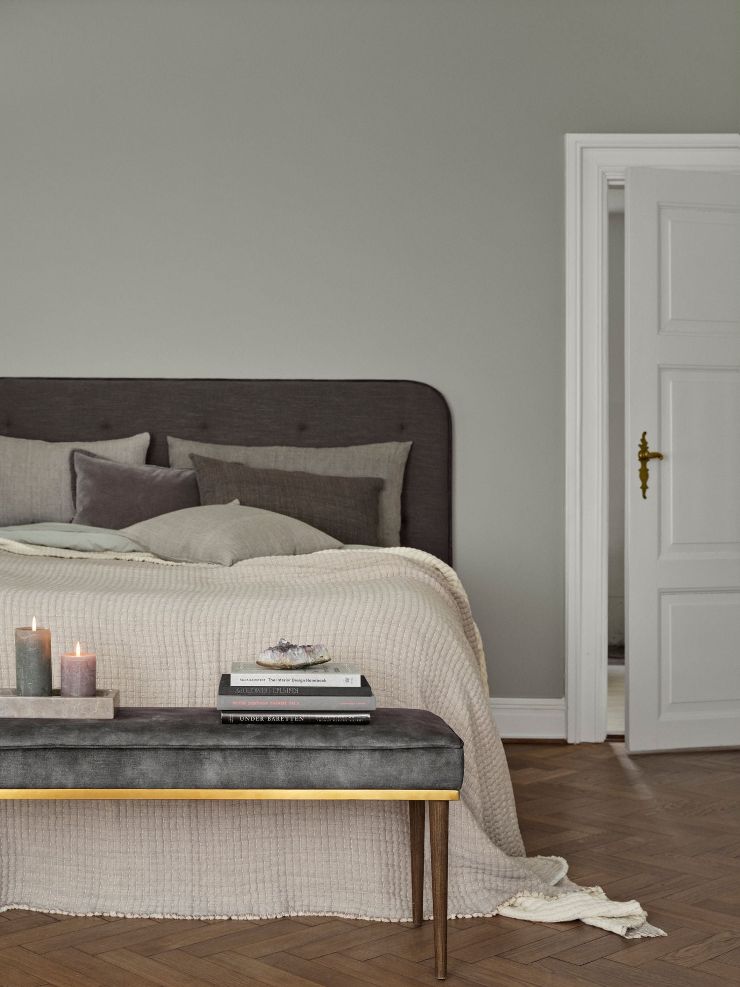 Fin redt seng med beige sengetæppe og forskellige nuancer af grå pyntepuder. 