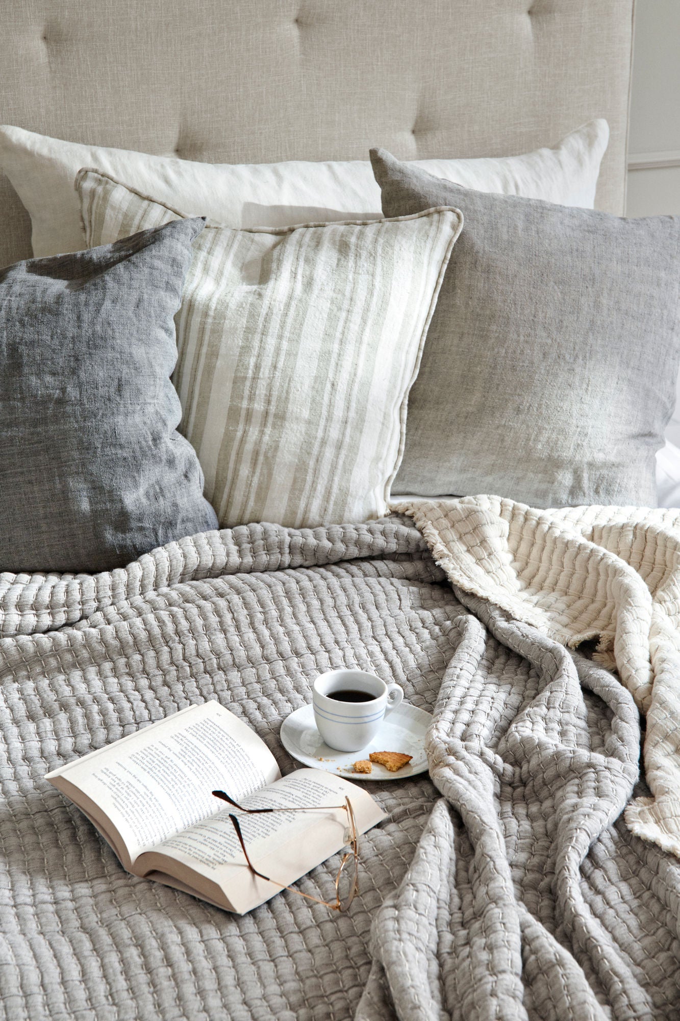 Seng med beige sengetæppe og forskellige nuancer af grå pyntepuder.