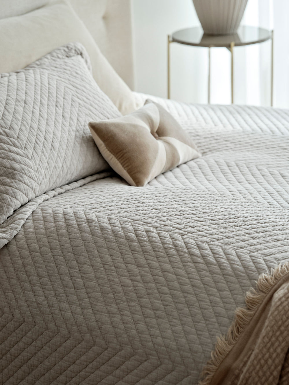 Seng redt med fint quiltet sengetæppe i beige og pyntepude i forskellige farver..