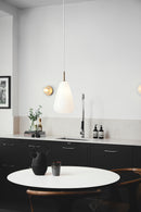 Dråbeformet pendel af opalglas med gyldent ophæng og hvid ledning, i køkkenmiljø over spisebord