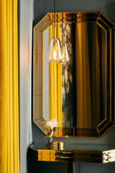 Dråbeformet pendel af gyldent glas, foran stort facetslebet spejl.