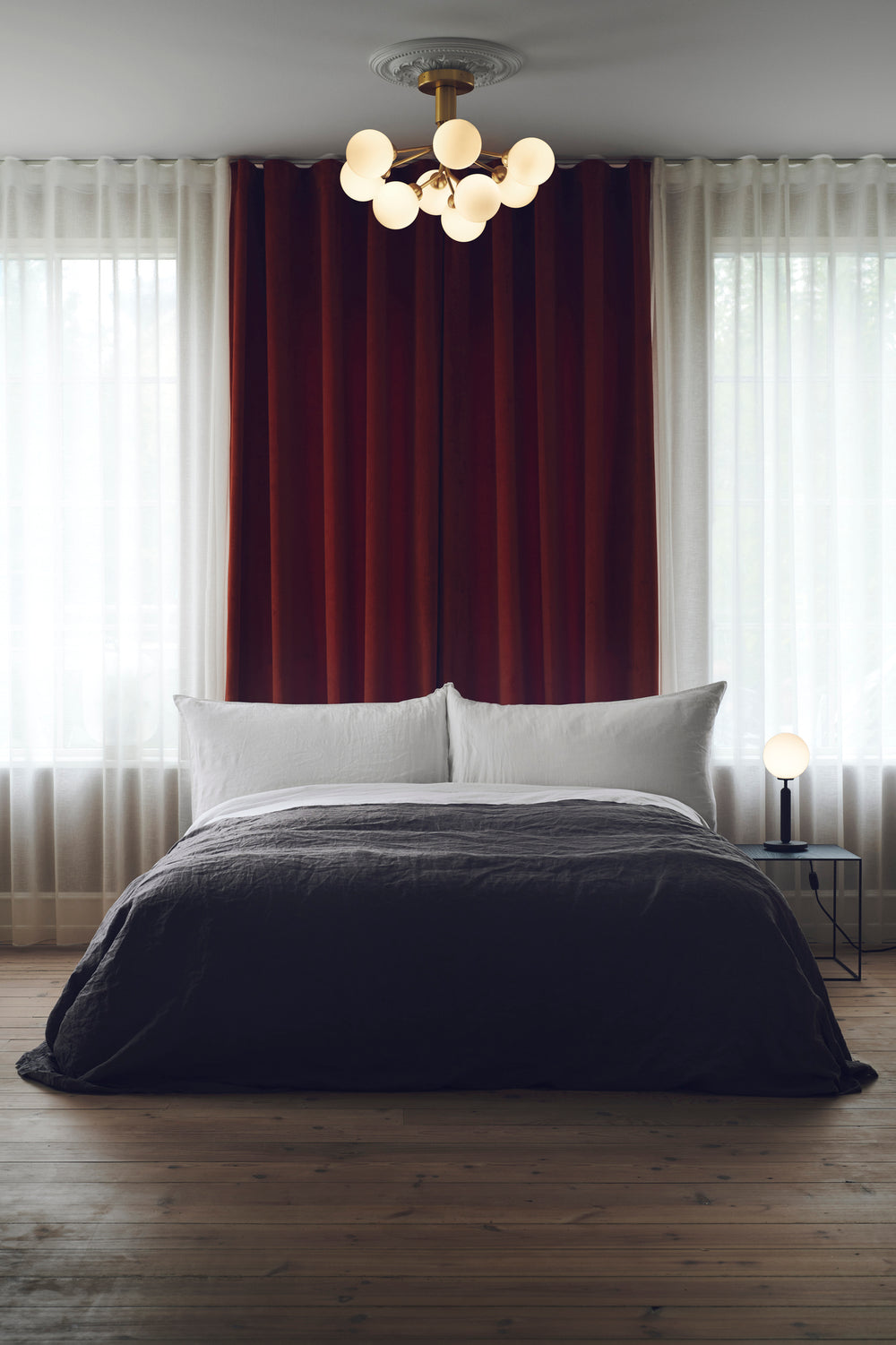 Lysekrone bestående af runde skærme i opalglas samt messingfarvet krone, over seng i soveværelse