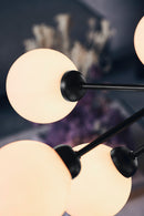 Close-up af lysekrone bestående af runde skærme i opalglas samt sort krone, i dagligstue miljø
