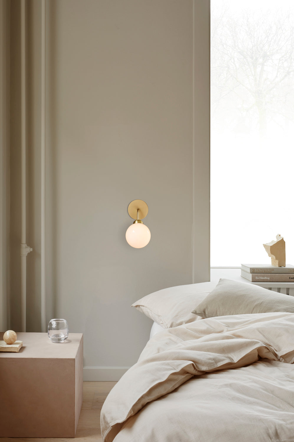 Væglampe med rund skærm af opalglas og messingfarvet stel, ved siden af seng i soveværelse