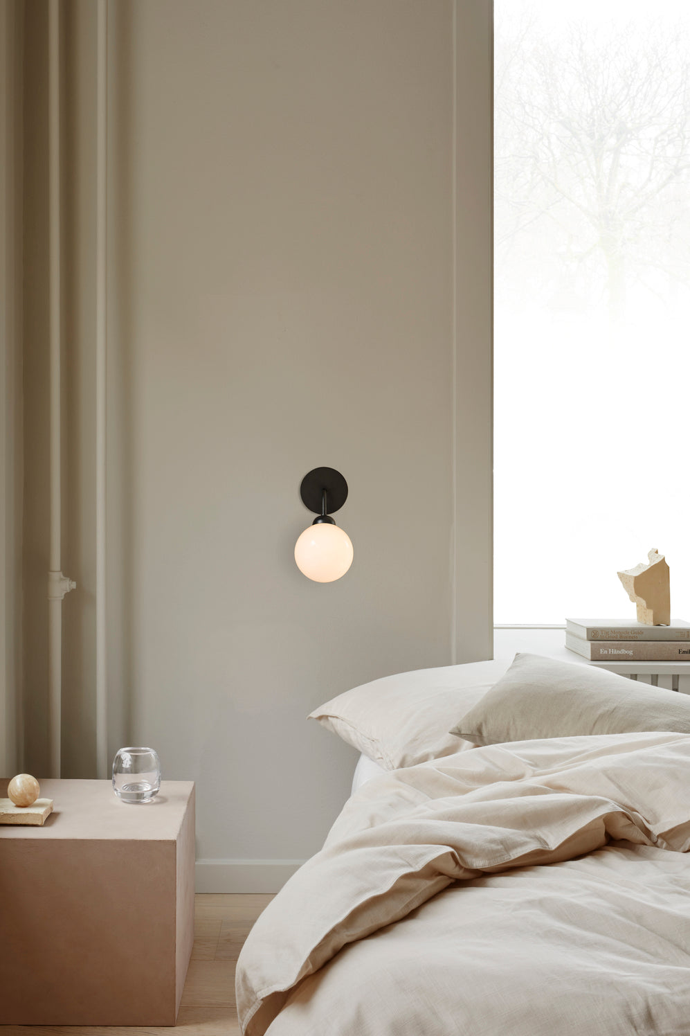 Væglampe med rund skærm af opalglas og sort stel, hængende ved siden af seng i soveværelse