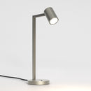 Stålfarvet bordlampe med justerbar hoved. Lampen har et enkelt design med firkantede linjer/vinkler.