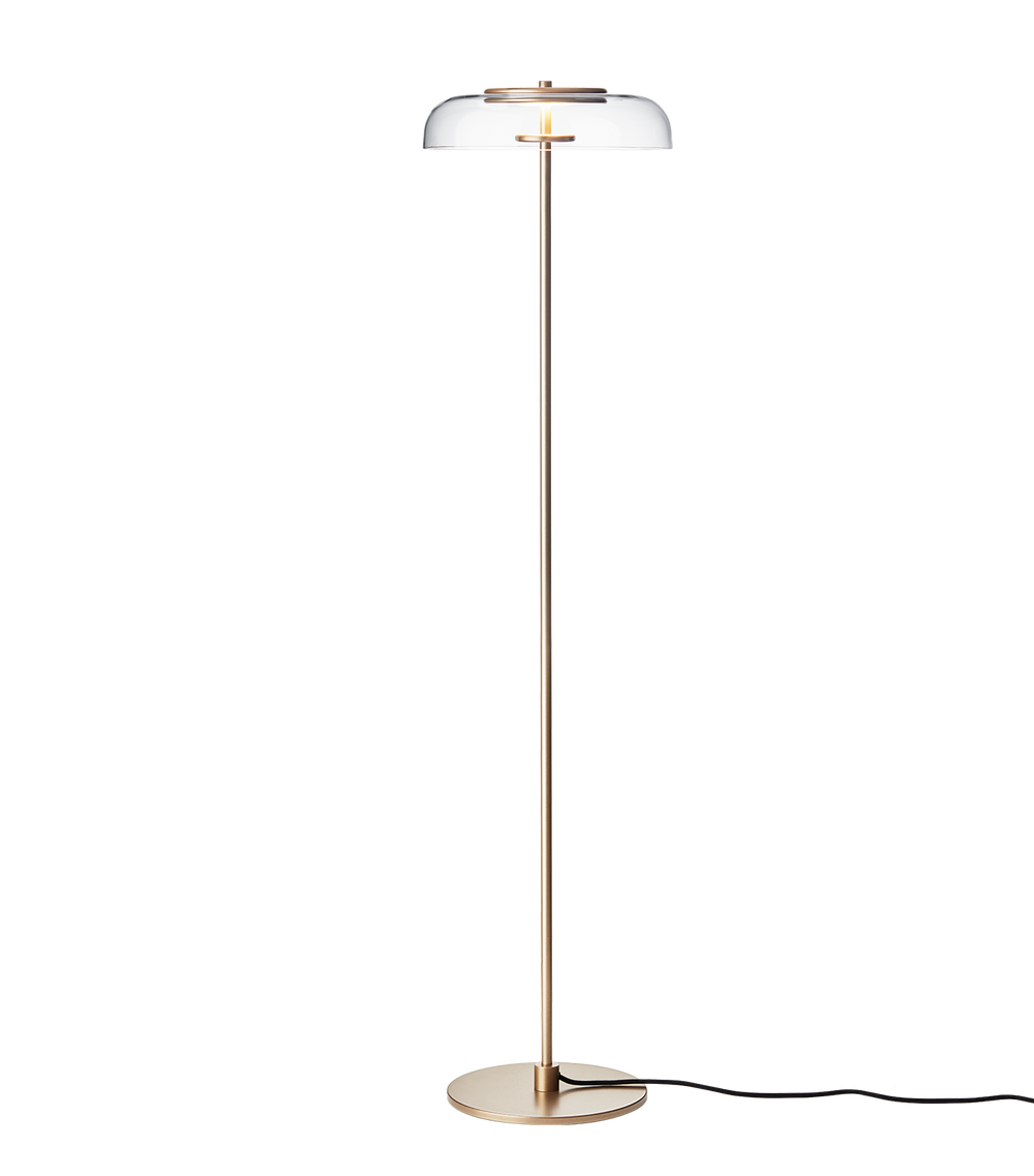 Gulvlampe med gyldent stel og fatning samt klar glasskærm, på hvid baggrund