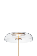 Gulvlampe med gyldent stel og fatning samt klar glasskærm, på hvid baggrund