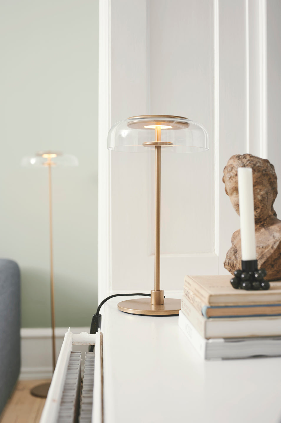 Bordlampe med gyldent stel og fatning samt glasskærm, i dagligstuemiljø