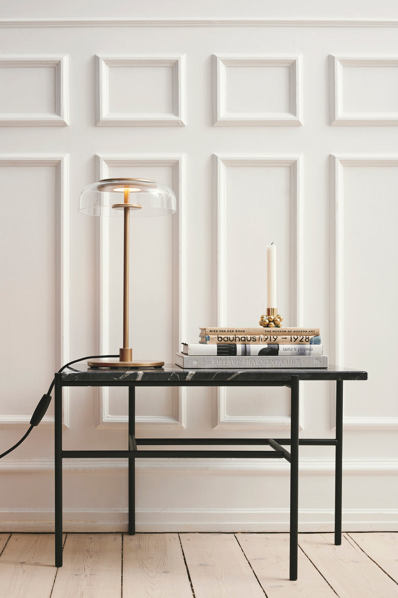 Bordlampe med gyldent stel og fatning samt glasskærm, i dagligstuemiljø