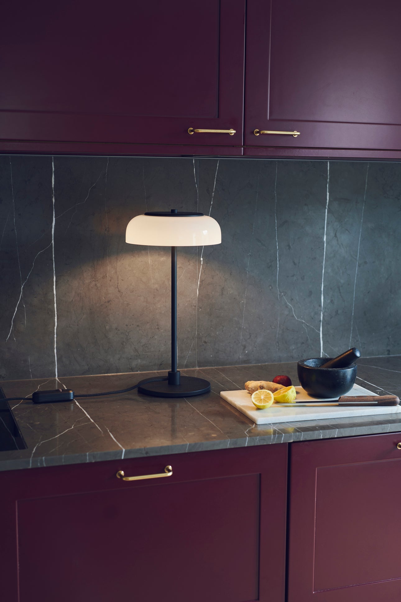 Bordlampe med sort stel og fatning og glasskærm i opalglas, i køkkenmiljø på køkkenbord